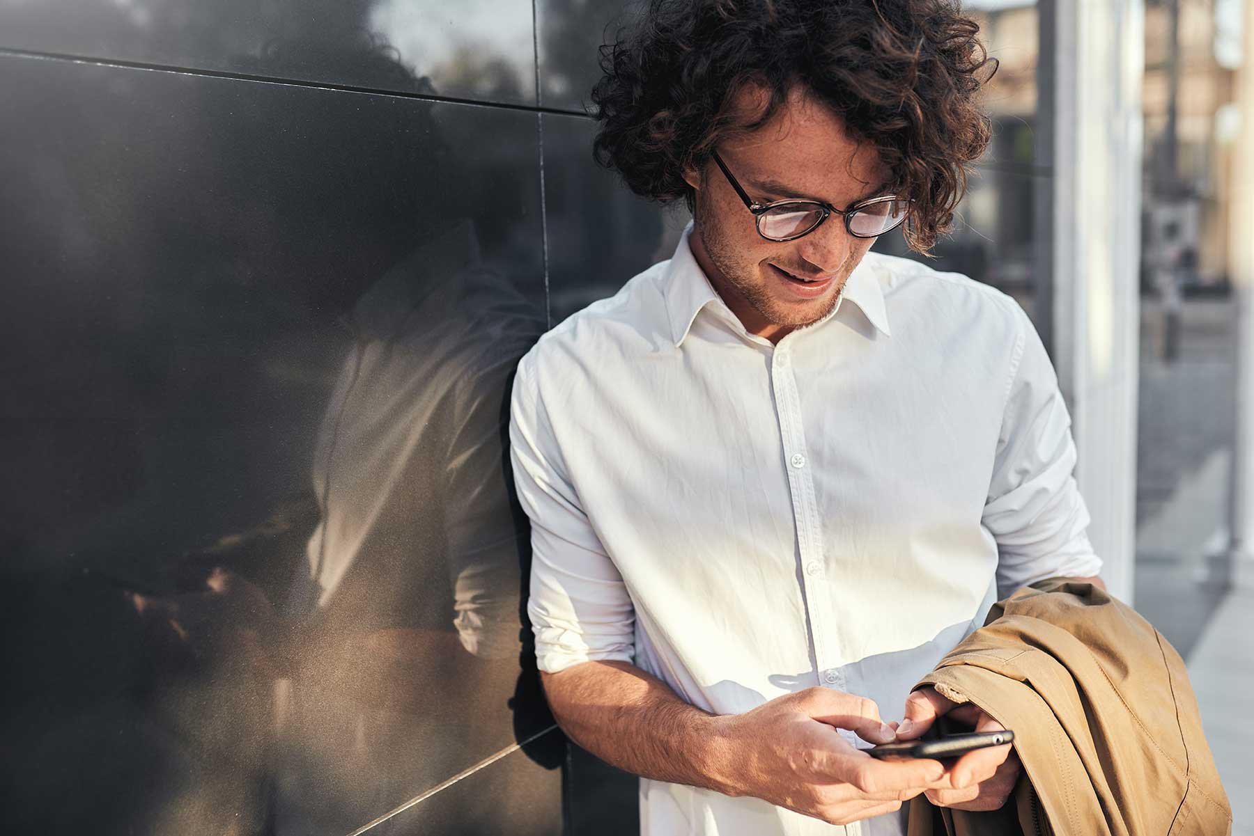 man med telefon lutar sig mot vägg